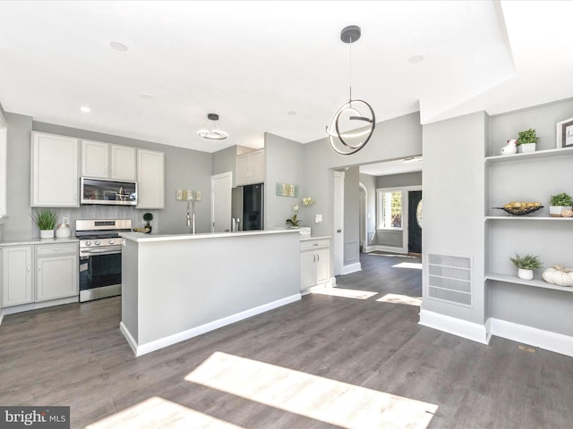 kitchen featuring dark wood-type flooring, appliances with stainless steel finishes, decorative light fixtures, and white cabinetry