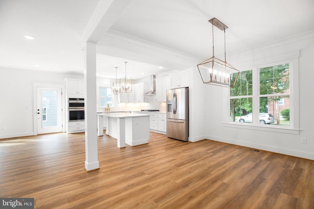 kitchen with appliances with stainless steel finishes, white cabinetry, wall chimney exhaust hood, decorative light fixtures, and a center island