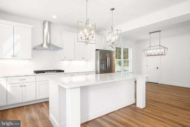 kitchen with white cabinets, wall chimney range hood, hardwood / wood-style floors, and stainless steel refrigerator with ice dispenser