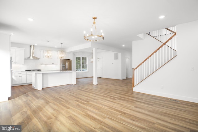 kitchen featuring stainless steel fridge, a center island with sink, light hardwood / wood-style floors, wall chimney exhaust hood, and decorative light fixtures