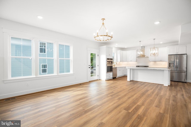 kitchen featuring wall chimney range hood, white cabinets, light wood-type flooring, decorative light fixtures, and stainless steel appliances