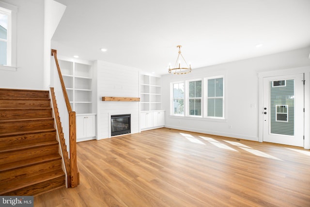 unfurnished living room with a large fireplace, a notable chandelier, light hardwood / wood-style flooring, and built in shelves