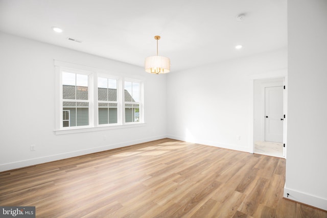 unfurnished room featuring a notable chandelier and light wood-type flooring