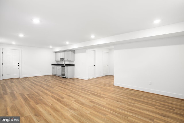 basement with sink, light hardwood / wood-style flooring, and beverage cooler