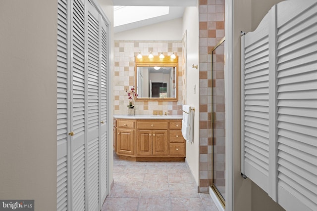 bathroom featuring tile walls, vanity, a shower with shower door, and lofted ceiling with skylight