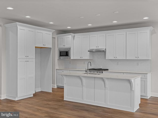 kitchen with stainless steel microwave, a center island with sink, white cabinets, and dark hardwood / wood-style flooring