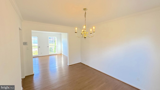 spare room featuring crown molding, wood-type flooring, and an inviting chandelier