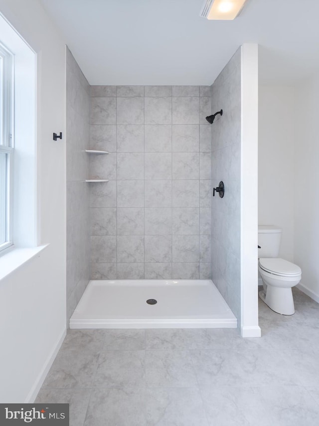 bathroom with toilet, tile patterned floors, and tiled shower