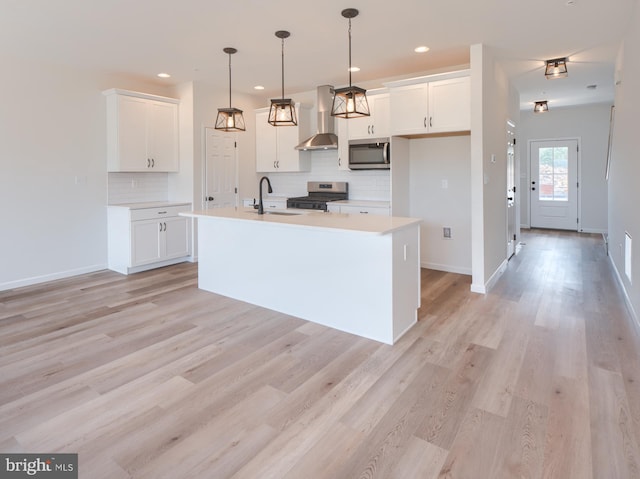 kitchen with white cabinetry, wall chimney range hood, appliances with stainless steel finishes, and a center island with sink