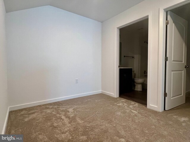 unfurnished bedroom with ensuite bath, light colored carpet, and vaulted ceiling