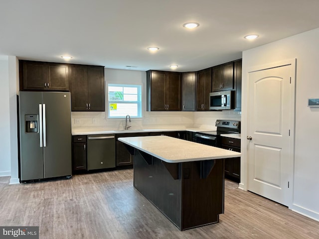 kitchen featuring appliances with stainless steel finishes, a kitchen bar, light wood-type flooring, sink, and a center island