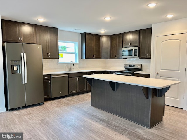 kitchen featuring a breakfast bar area, a center island, dark brown cabinetry, appliances with stainless steel finishes, and light hardwood / wood-style floors