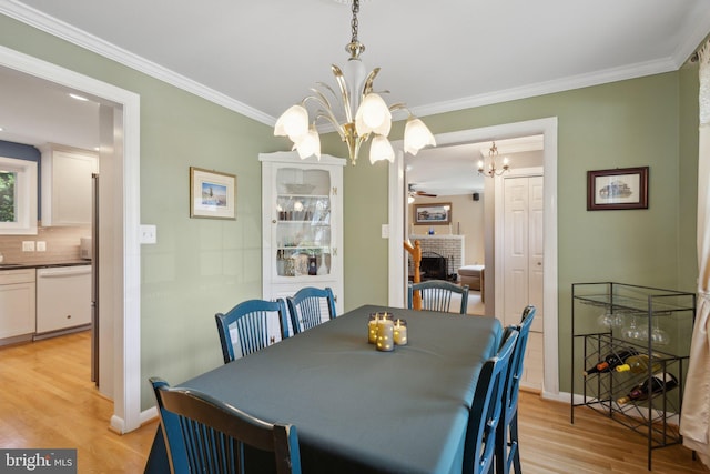 dining area featuring ceiling fan with notable chandelier, light wood-type flooring, ornamental molding, and a brick fireplace