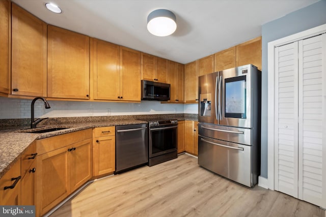 kitchen featuring light hardwood / wood-style floors, sink, appliances with stainless steel finishes, and dark stone counters