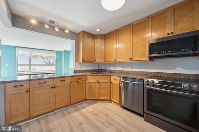 kitchen featuring sink, light hardwood / wood-style flooring, backsplash, dark stone counters, and appliances with stainless steel finishes