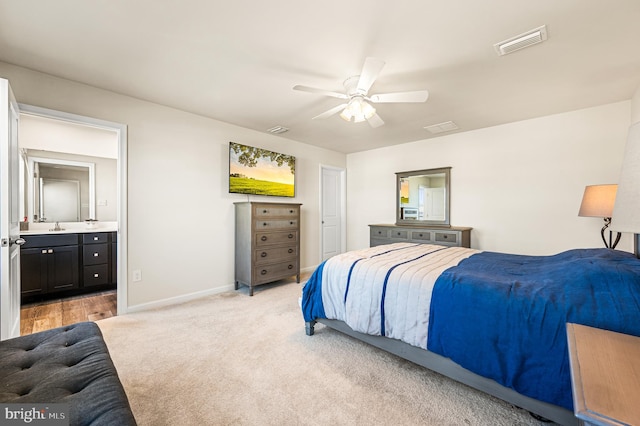 bedroom with ceiling fan, light colored carpet, sink, and ensuite bath