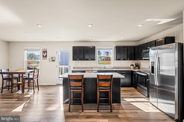 kitchen featuring a center island, light stone counters, light hardwood / wood-style flooring, a kitchen bar, and appliances with stainless steel finishes