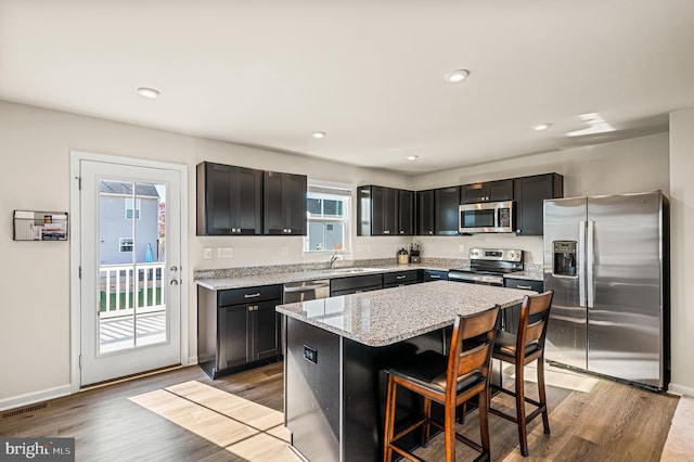 kitchen featuring a center island, a kitchen breakfast bar, a wealth of natural light, appliances with stainless steel finishes, and light stone counters