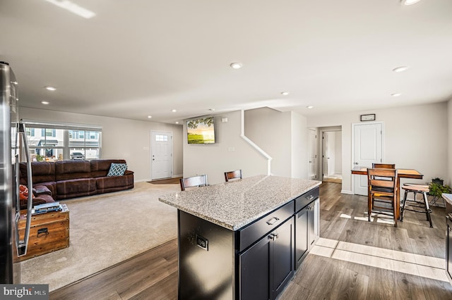 kitchen featuring stainless steel refrigerator, light stone countertops, a kitchen island, and light wood-type flooring