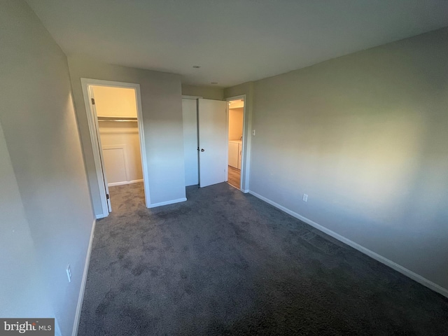 unfurnished bedroom featuring a closet, a walk in closet, and dark colored carpet