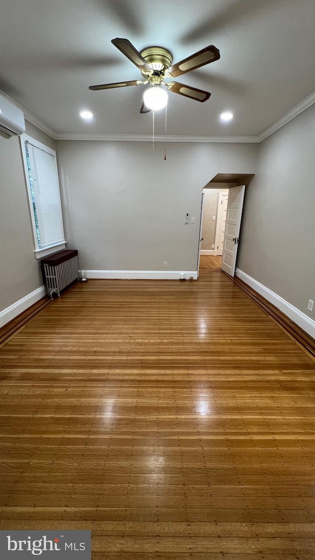 unfurnished room featuring radiator heating unit, ceiling fan, a wall unit AC, crown molding, and hardwood / wood-style flooring