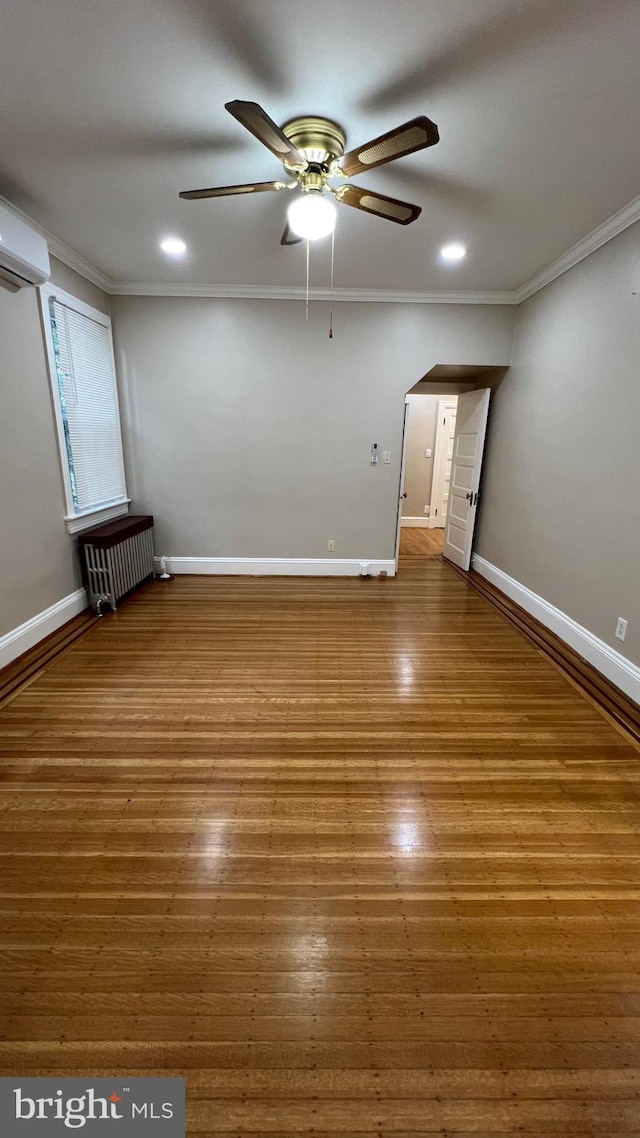 spare room featuring a wall mounted air conditioner, radiator, ceiling fan, crown molding, and hardwood / wood-style flooring