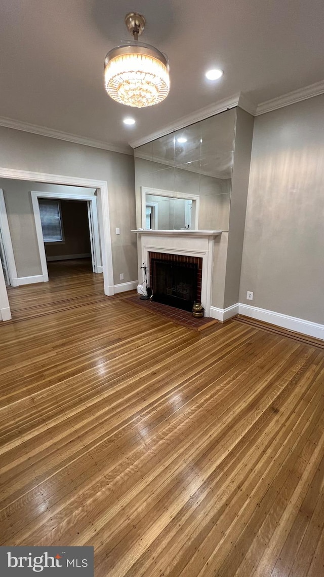 unfurnished living room with ornamental molding, a brick fireplace, and hardwood / wood-style floors