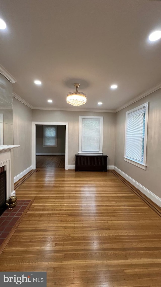 unfurnished living room with radiator, wood-type flooring, ornamental molding, and a tile fireplace