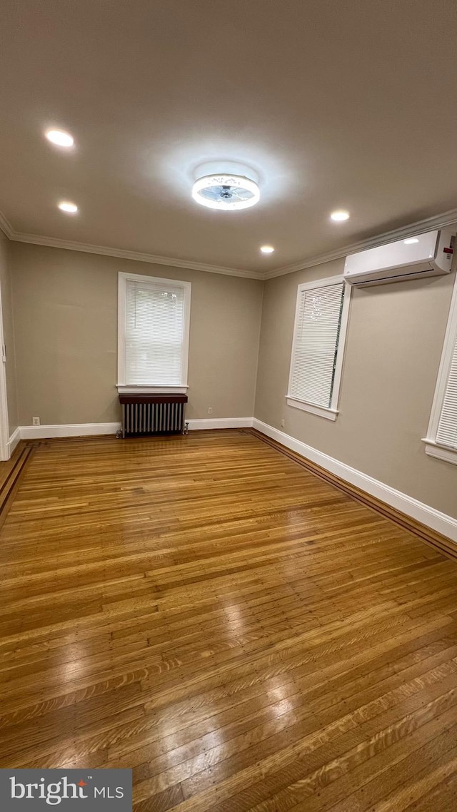 empty room featuring an AC wall unit, ornamental molding, hardwood / wood-style floors, and radiator