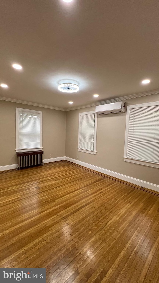 unfurnished room featuring radiator, hardwood / wood-style flooring, a wall mounted AC, and ornamental molding