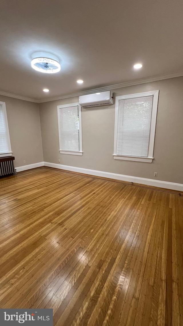 spare room featuring radiator, crown molding, a wall mounted AC, and hardwood / wood-style floors