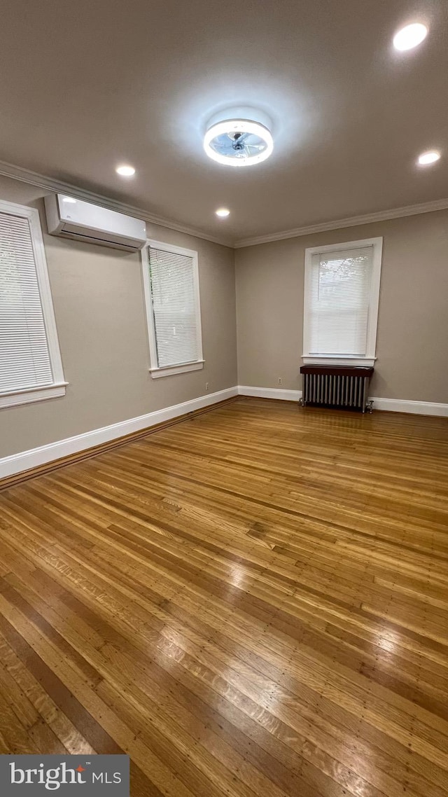 unfurnished room featuring a wall mounted air conditioner, ornamental molding, radiator, and wood-type flooring