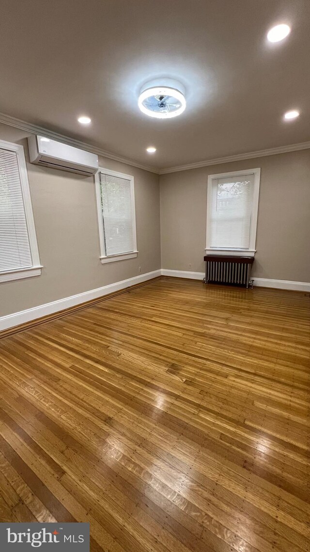 unfurnished room with ornamental molding, hardwood / wood-style floors, a wall mounted AC, and radiator heating unit