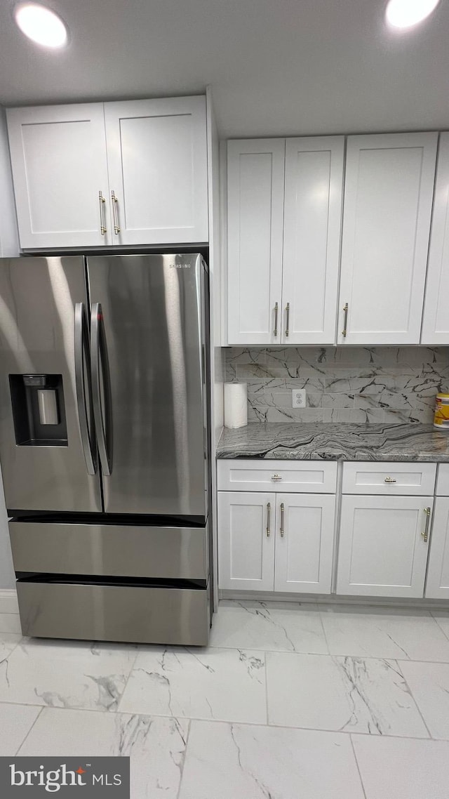 kitchen featuring white cabinetry, stainless steel fridge, tasteful backsplash, and dark stone counters