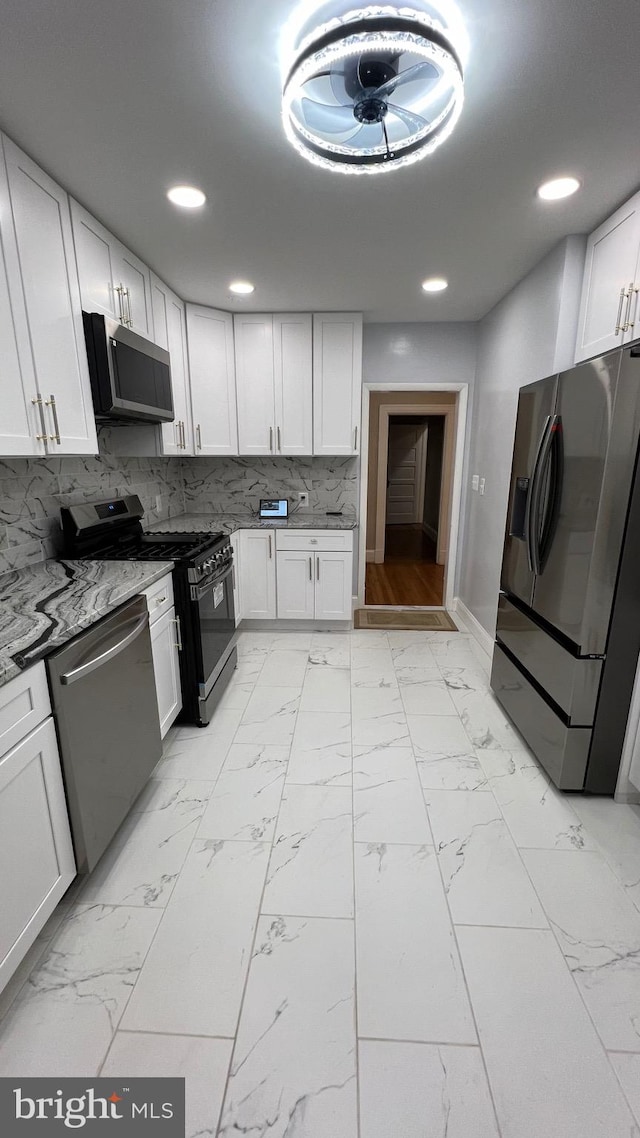 kitchen featuring appliances with stainless steel finishes, decorative backsplash, white cabinets, and dark stone counters