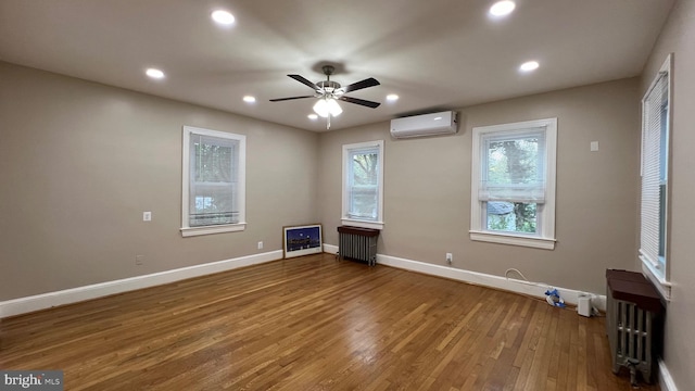 empty room featuring ceiling fan, an AC wall unit, wood-type flooring, and radiator heating unit