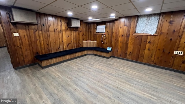 basement featuring a wall mounted AC, light hardwood / wood-style flooring, a paneled ceiling, and wood walls