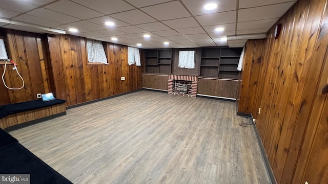 basement featuring hardwood / wood-style floors, a drop ceiling, a brick fireplace, and wood walls