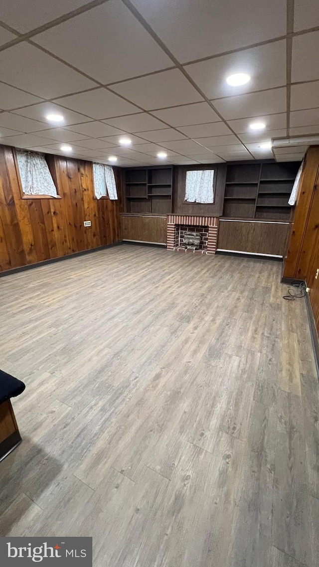 basement with a paneled ceiling, a healthy amount of sunlight, wood walls, and hardwood / wood-style floors