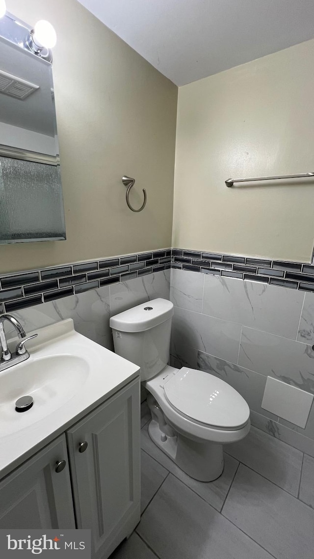 bathroom with vanity, toilet, tile patterned floors, and tile walls