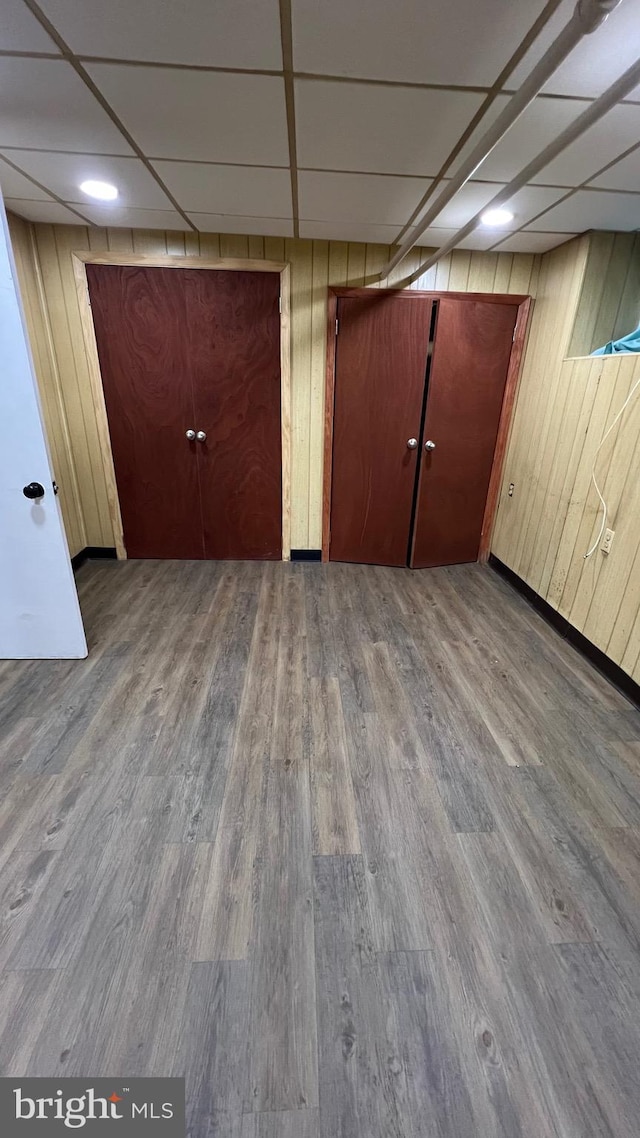 unfurnished bedroom featuring hardwood / wood-style floors, a paneled ceiling, and wood walls