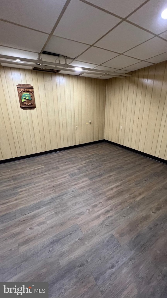 basement featuring a paneled ceiling, hardwood / wood-style flooring, and wooden walls