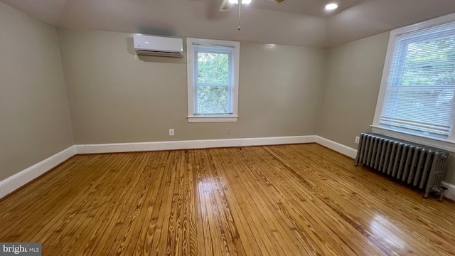 spare room with plenty of natural light, a wall mounted AC, light hardwood / wood-style floors, and radiator