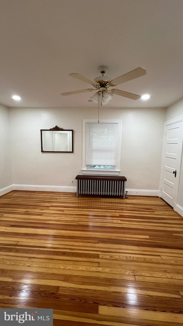 spare room featuring hardwood / wood-style floors, radiator, and ceiling fan