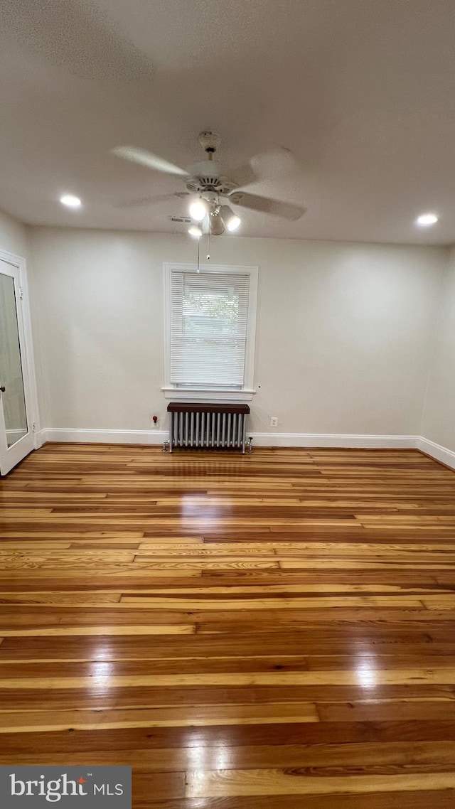 spare room featuring ceiling fan, radiator heating unit, and hardwood / wood-style floors