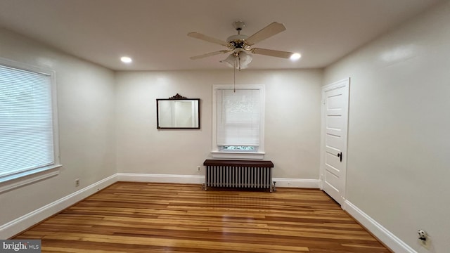 unfurnished room with ceiling fan, radiator heating unit, light hardwood / wood-style floors, and plenty of natural light