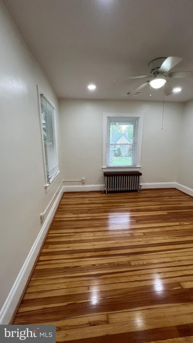 unfurnished room with hardwood / wood-style floors, radiator, and ceiling fan