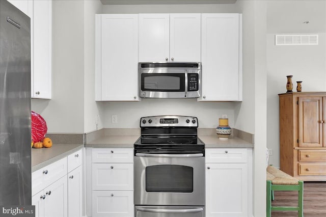 kitchen with white cabinetry, stainless steel appliances, and hardwood / wood-style floors