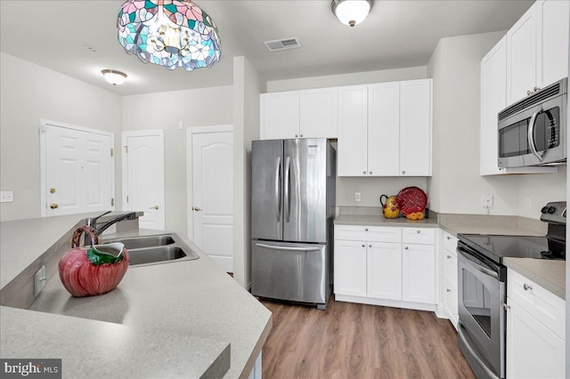 kitchen featuring hardwood / wood-style floors, white cabinets, sink, decorative light fixtures, and stainless steel appliances