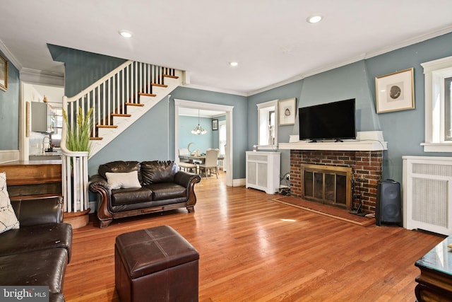 living room with wood-type flooring, radiator heating unit, ornamental molding, a notable chandelier, and a fireplace